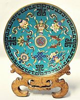 Front view of cloisonné plate on stand showing turquoise enamel ground, key-fret border and central motifs.