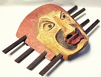 Angled front view showing carved facial features, red backing and horizontal wooden rods