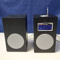 Front and side view of the two Tivoli Audio Model 10 units showcasing the wood-encased main clock radio with metal speaker grille, digital blue display, and companion speaker.
