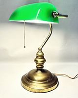 Full view of the vintage bankers desk lamp showing the green glass shade and brass body illuminated.