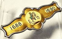 Close-up image of a vintage Orange Lodge membership badge number 1690 with yellow background, silver edges, and central riding figure illustration.