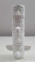 Stacked view of four white ceramic shot glasses forming a totem pole about 7.75 inches tall, showing entire assembled set with detailed facial features and wings on bottom piece.