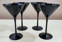 Four black martini glasses grouped together showing their shape and glossy finish.