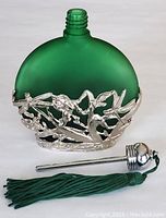 Green frosted glass perfume bottle without stopper, showing silver-tone floral and leaf metal overlay near base.