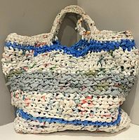 Front view of handmade tote bag made from woven plastic shopping bags showing its texture, colors, and handles.