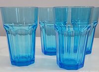 Four turquoise tempered glass beverage glasses shown from the side, highlighting shape, color, and fluted vertical design.