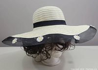 Ivory wide brim sun hat displayed on mannequin head, showing black mesh brim with white daisy flower decorations from side angle.