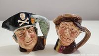 Front view of Long John Silver and Arry jugs showing detailed facial paint, pirate hat with skull and crossbones, and parrot on Long John Silver's shoulder.