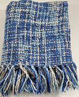 Close-up of folded knit throw blanket showing blue, white, and gray plaid pattern and fringe detail