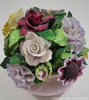 Photo showing top view of colorful porcelain floral arrangement with roses, pansies and other flowers, glossy finish, on light pink base.