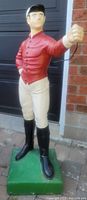 Full front view of the vintage cement horse jockey lawn statue showing the red jacket, white pants, black boots on green base.