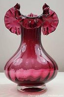 Front view of deep cranberry glass vase showing bulbous base and ruffled flared top.