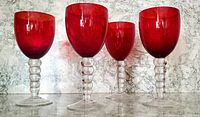 Four vintage red glass goblets with clear beehive-shaped stems side by side, showing front view and differences in bowl size