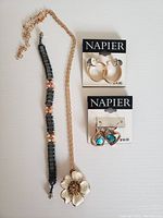 Two new pairs of Napier pierced earrings, a mother of pearl flower pendant necklace, and a black beads and stones bracelet displayed on a white background.