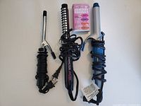Two curling irons and one curling brush with cords wrapped around handles, viewed from front on white background.