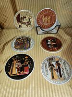 Photo of six round Egyptian coasters with different detailed designs and a matching white holder on striped fabric.