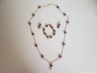 Photo showing red heart-shaped necklace, bracelet, and earrings with floral designs on a gold-tone chain.
