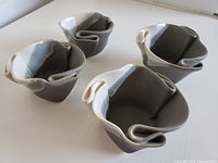 Four small ceramic serving cups with folded design and combination of gray, white, and pink matte glazes, shown grouped together from top and side angles.