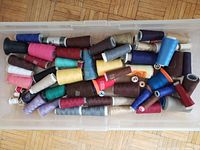 Top-down view of clear container filled with over 70 colorful sewing thread spools in various colors and sizes.