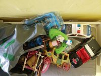 Various Playmobil toys including a yellow coach carriage, police car, and a black vehicle with red detailing and cross markings, along with other toy pieces and accessories in a box.
