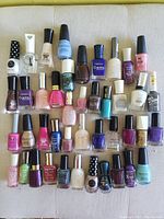 Photo showing 32 nail polish bottles of various colors, finishes, and brands laid out on a white surface.