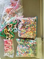 Photo showing multiple bags filled with assorted colorful beads and a collection of beaded necklaces in various colors and styles on a neutral background.
