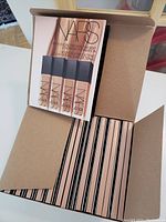 Open box of 25 NARS Natural Longwear Foundation sample packs showing multiple units packed neatly inside, each pack containing four foundation sample vials.