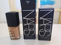 Two NARS Sheer Glow Foundation bottles with black caps and medium/dark shade visible inside next to their original packaging boxes.