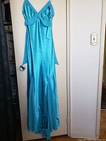 Full view of a baby blue floor-length gown hanging on a white door, showing its flowing skirt and satin fabric.