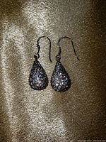 Pair of teardrop-shaped pearl drop diamond cluster earrings on a fabric background