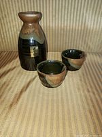 Photo showing the full saki set including one bottle and two cups arranged on a striped fabric background.