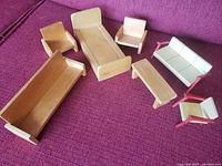 Full set of unfinished wooden dollhouse furniture on a purple surface including bed, bench, rocking chairs, armchair, sofa, coffee table.
