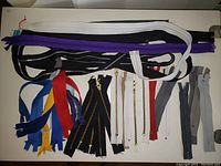 Top view of assorted zippers arranged on white surface showing variety of lengths, colors, and teeth materials.