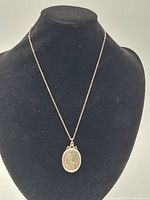 Silver oval engraved vintage locket hanging on black display bust, showing entire necklace and pendant.