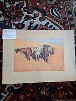 Photo showing the full mounted print of a Western scene with horses and a wagon on a patterned carpet, including a label.