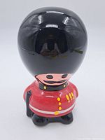 Front view showing the ceramic British Bobby figure piggy bank in vibrant red uniform and tall black helmet.