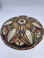 Top view of a coloured leaded glass dome light shade with a floral and geometric pattern in amber, cream, green, and brown.
