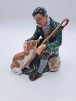 Front side view showing the man seated with shepherd's crook and dog looking up at him.