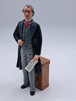 Front view of Royal Doulton figurine of Sir John A. MacDonald standing and holding a paper beside a brown pedestal.