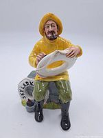 Front view of the Doulton "The Boatman" figurine showing the man seated holding a white life ring with 'SKYLARK' painted on it.