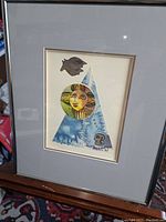 Framed signed artwork featuring a blue triangular shape with a colorful circular face, a bird, and abstract shapes.