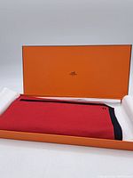 Orange Hermes presentation box open with folded red and black scarf inside.