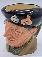 Side-left angle showing the detailed face, black cap with insignia, and handle on the rear.