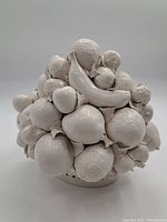 Front view of the spherical porcelain fruit bowl showing multiple sculpted fruits such as banana and orange in white.