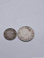 Two Newfoundland silver coins placed side by side on a plain white surface, showing the reverse sides with denomination and years 10 cents 1894 and 20 cents 1896.