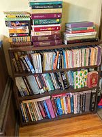 Wooden bookshelf fully stocked with assorted books of various colors and sizes, mostly paperback.