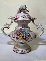 Full front view of porcelain covered vase with sculpted handles and floral motifs