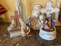 Five religious ceramic figurines including cross with doves, Madonna and Child bust, small angel and cherub, and Holy Family figurine with cross and inscription.