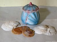 Front view of blue and pink ceramic seashell-shaped jar with surrounding white and brown scallop shells
