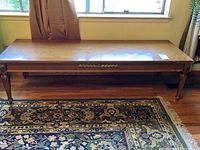 Full view of long rectangular wooden coffee table in a room with patterned area rug below and window behind.